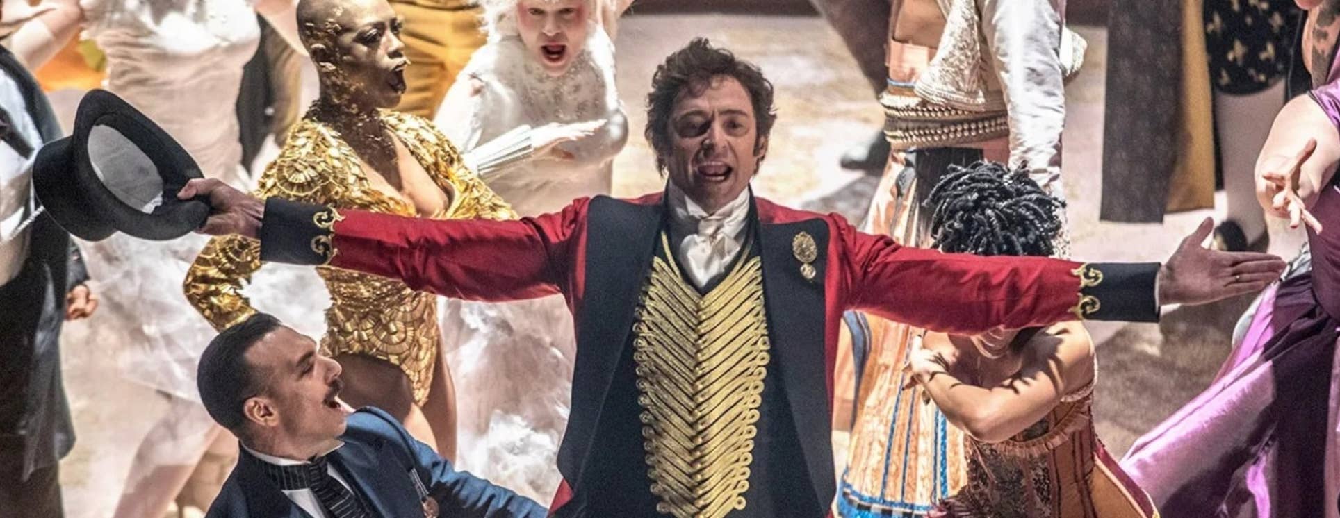People in period costumes dance in a dramatic scene, including a curly-haired man in a red coat and gold details.